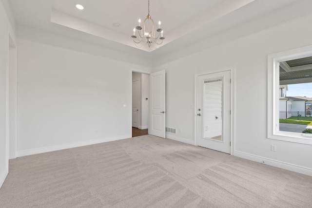 interior space with a tray ceiling, an inviting chandelier, and light colored carpet