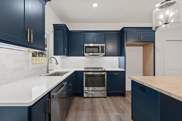 kitchen with sink, blue cabinets, hanging light fixtures, and appliances with stainless steel finishes