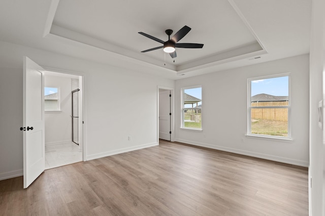 empty room with light hardwood / wood-style flooring, a raised ceiling, and ceiling fan