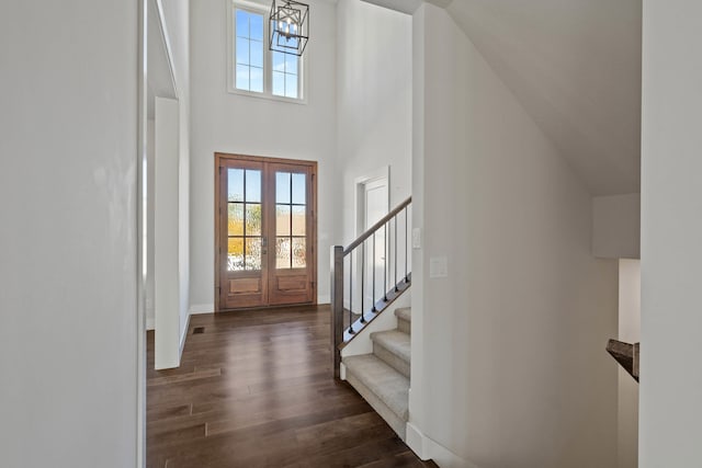 foyer entrance featuring a notable chandelier, a towering ceiling, dark wood-type flooring, and french doors