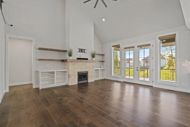 unfurnished living room with french doors, high vaulted ceiling, a stone fireplace, and dark wood-type flooring