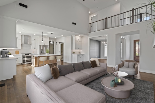 living room featuring a barn door, a towering ceiling, dark wood-type flooring, and an inviting chandelier