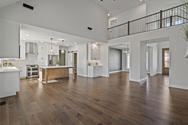 living room featuring dark wood-type flooring, sink, a barn door, a towering ceiling, and a notable chandelier