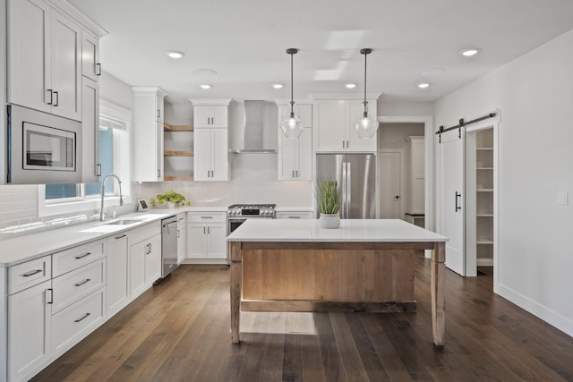 kitchen with a center island, wall chimney exhaust hood, hanging light fixtures, stainless steel appliances, and a barn door