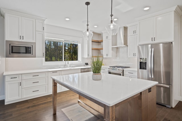 kitchen featuring dark hardwood / wood-style flooring, stainless steel appliances, wall chimney range hood, pendant lighting, and white cabinetry