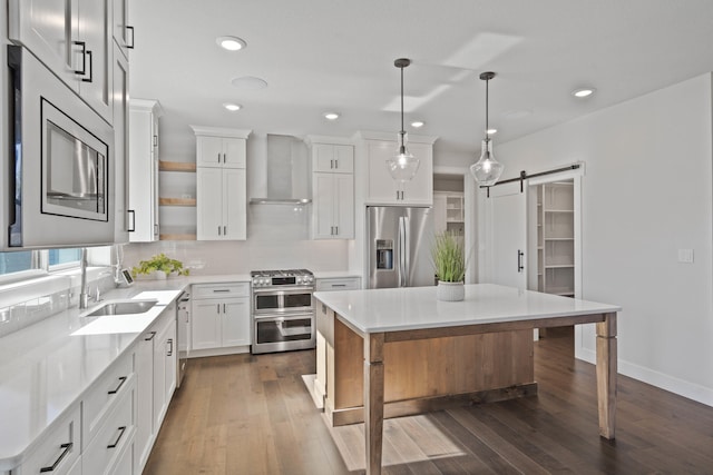 kitchen featuring white cabinetry, wall chimney range hood, a barn door, pendant lighting, and appliances with stainless steel finishes