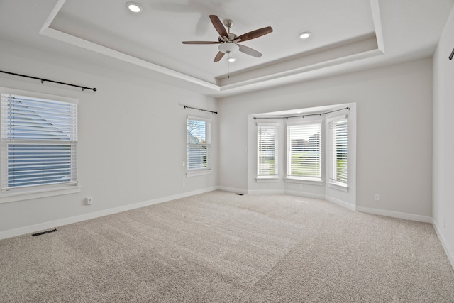 empty room featuring a tray ceiling, ceiling fan, and carpet floors