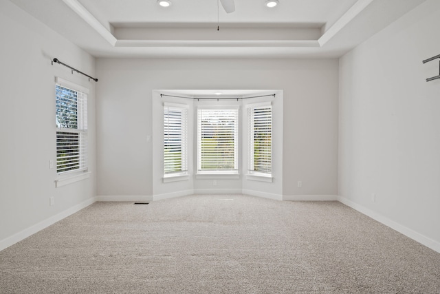 empty room with light carpet, a raised ceiling, and ceiling fan