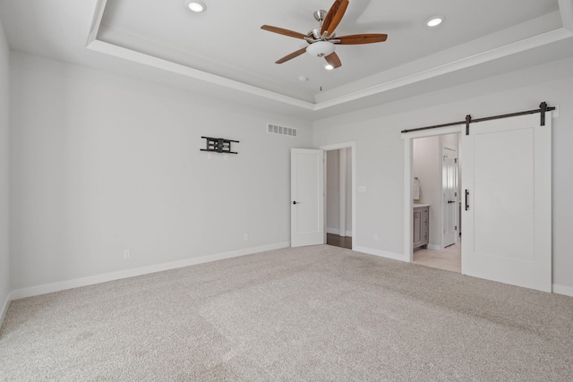 spare room featuring a raised ceiling, a barn door, ceiling fan, and light colored carpet