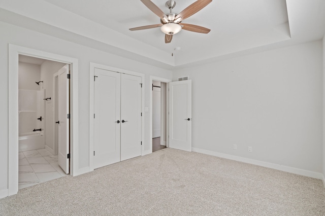 unfurnished bedroom with ceiling fan, a raised ceiling, light colored carpet, and connected bathroom