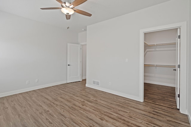 unfurnished bedroom with hardwood / wood-style flooring, ceiling fan, a walk in closet, and a closet