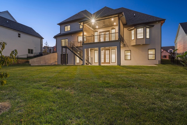 back house at dusk with a balcony, a yard, and french doors