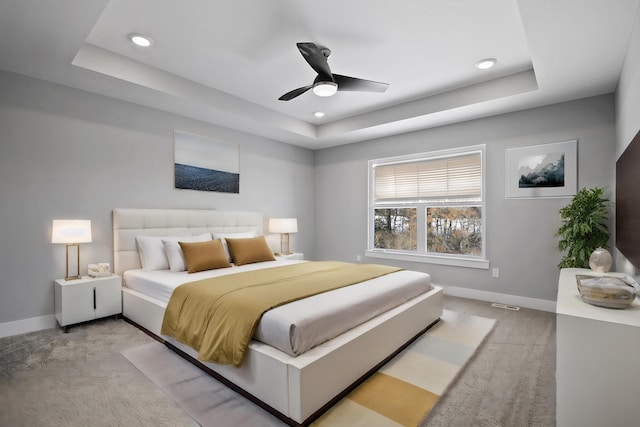 bedroom with light carpet, a raised ceiling, and ceiling fan