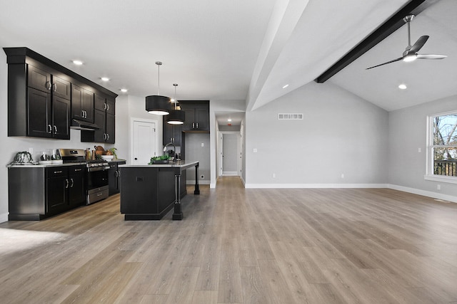 kitchen with pendant lighting, a kitchen island with sink, lofted ceiling with beams, stainless steel range with gas cooktop, and ceiling fan