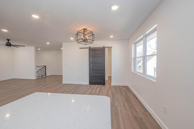 spare room featuring recessed lighting, a barn door, baseboards, and wood finished floors