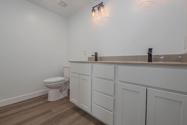 bathroom featuring visible vents, toilet, a sink, wood finished floors, and double vanity