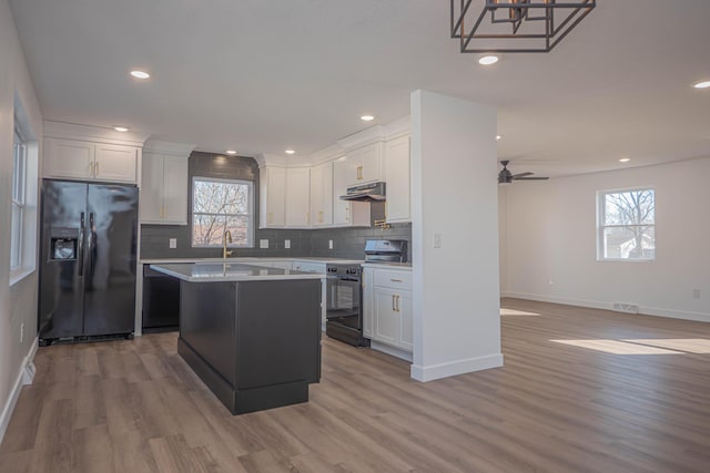 kitchen with black fridge, under cabinet range hood, backsplash, electric range oven, and white cabinetry