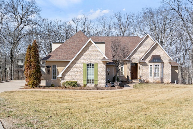 view of front of house with stone siding, roof with shingles, and a front lawn