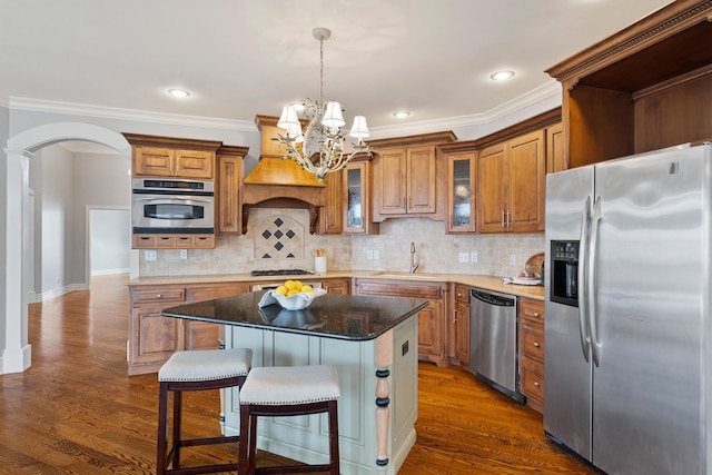 kitchen with arched walkways, dark wood-style flooring, a sink, appliances with stainless steel finishes, and brown cabinetry