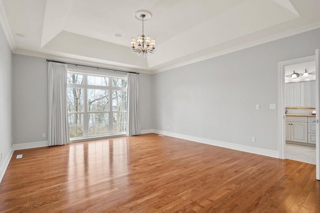 spare room featuring light wood-style flooring, a notable chandelier, baseboards, a raised ceiling, and crown molding