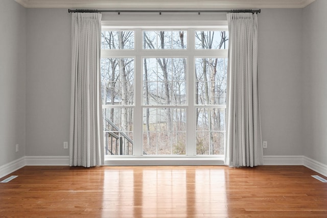 spare room with wood finished floors, visible vents, and baseboards