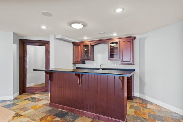 kitchen featuring stone tile flooring, baseboards, a kitchen breakfast bar, and dark brown cabinets