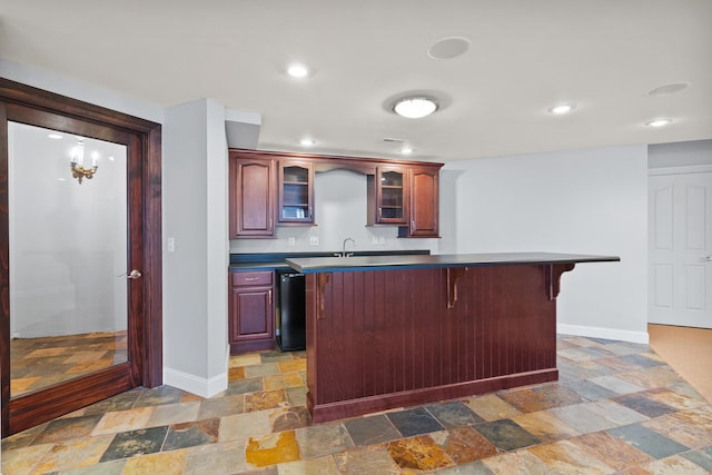 kitchen with reddish brown cabinets, a breakfast bar area, stone tile flooring, and baseboards