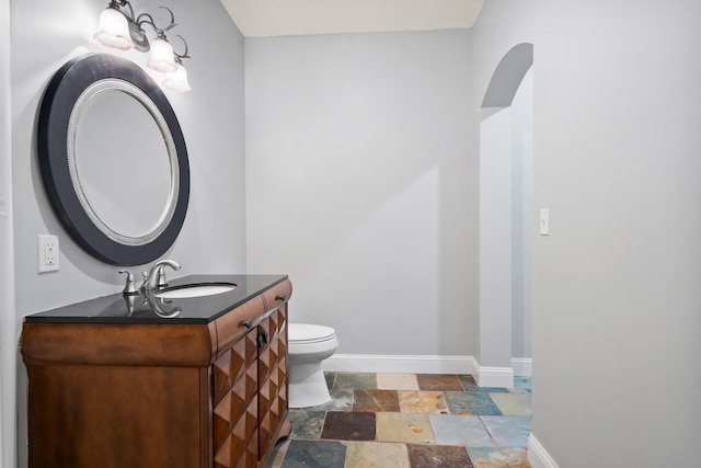 half bathroom featuring baseboards, toilet, vanity, and stone tile floors