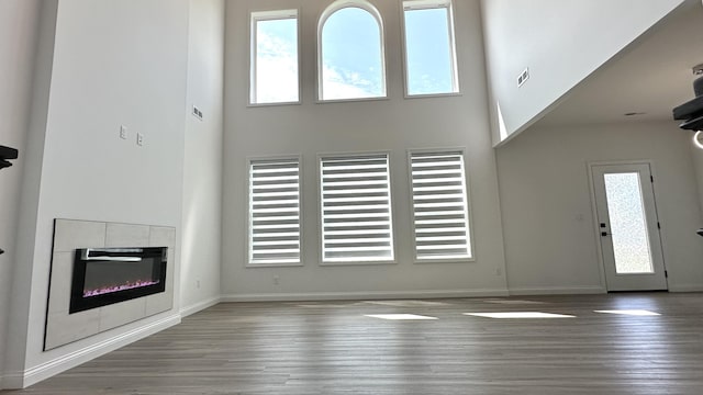 unfurnished living room with a tile fireplace, wood-type flooring, a towering ceiling, and plenty of natural light