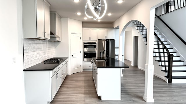 kitchen featuring tasteful backsplash, stainless steel appliances, a kitchen island with sink, dark wood-type flooring, and range hood