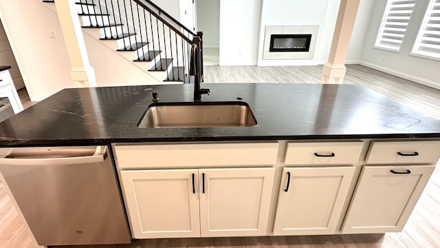 kitchen with dark stone countertops, sink, stainless steel dishwasher, and light hardwood / wood-style floors