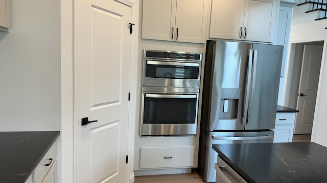 kitchen featuring dark stone counters, white cabinetry, stainless steel appliances, and light wood-type flooring