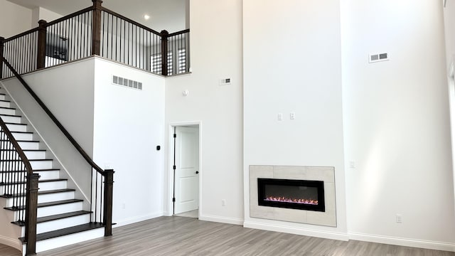 unfurnished living room featuring a fireplace, a towering ceiling, and hardwood / wood-style flooring