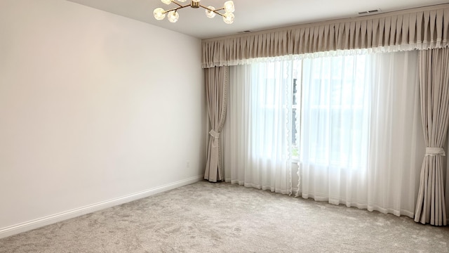 empty room with carpet flooring, a notable chandelier, and a healthy amount of sunlight