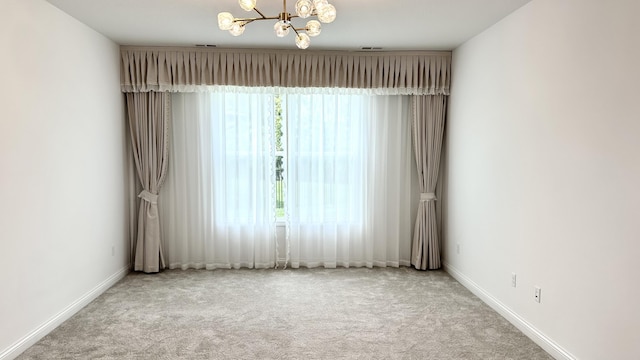 carpeted empty room featuring a healthy amount of sunlight and a notable chandelier