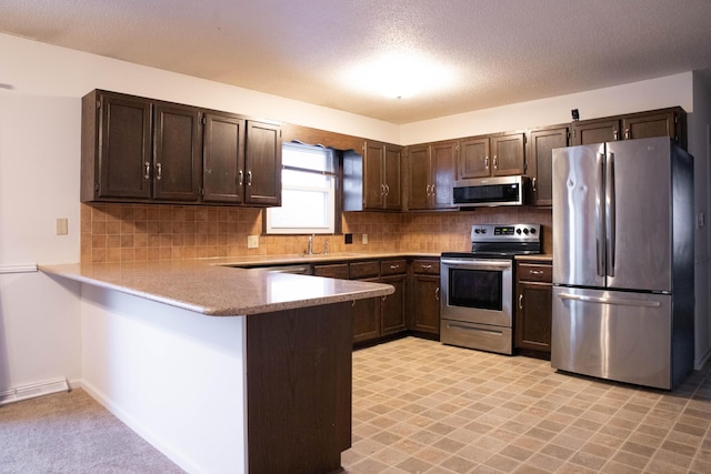 kitchen with kitchen peninsula, appliances with stainless steel finishes, tasteful backsplash, and dark brown cabinetry