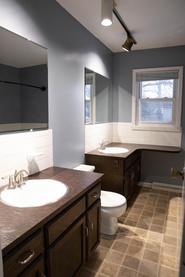 bathroom featuring track lighting, toilet, vanity, and decorative backsplash