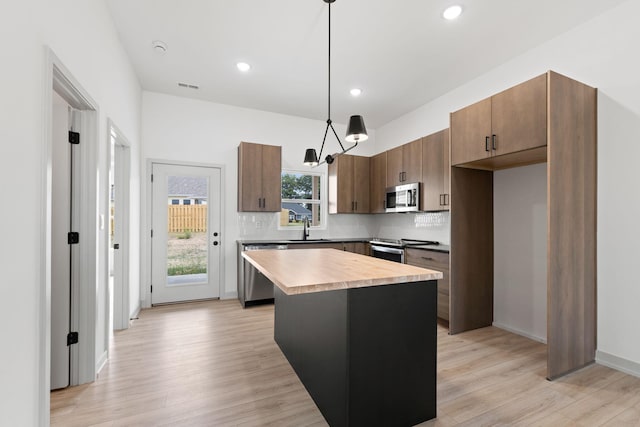 kitchen featuring sink, a center island, hanging light fixtures, appliances with stainless steel finishes, and light wood-type flooring