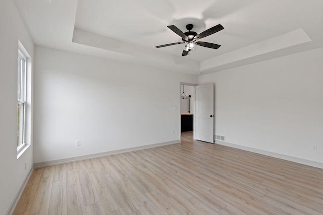 empty room featuring light hardwood / wood-style flooring, a raised ceiling, and ceiling fan