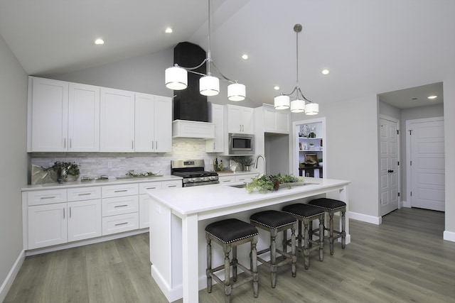 kitchen featuring appliances with stainless steel finishes, sink, a center island with sink, decorative light fixtures, and white cabinetry