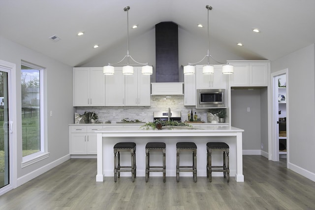 kitchen featuring a breakfast bar, a kitchen island with sink, stainless steel microwave, and white cabinets