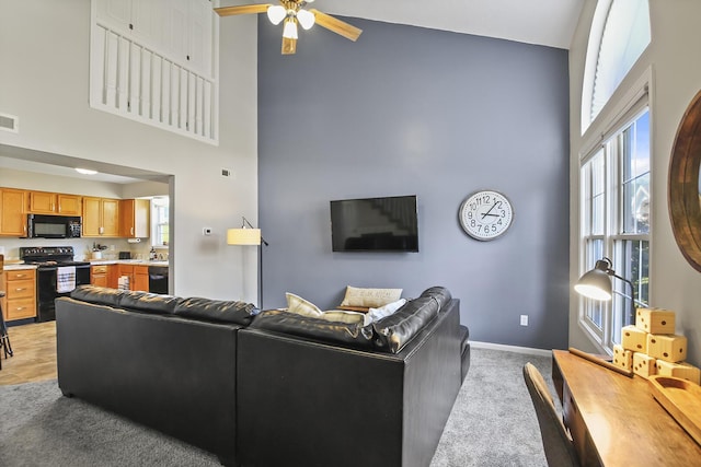 living room with light carpet, ceiling fan, plenty of natural light, and a high ceiling