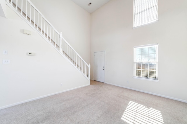 unfurnished living room with a towering ceiling and light carpet