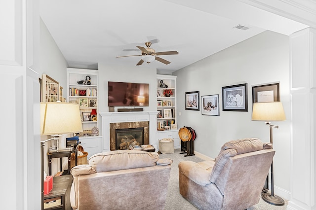 carpeted living room with a tile fireplace, built in shelves, and ceiling fan