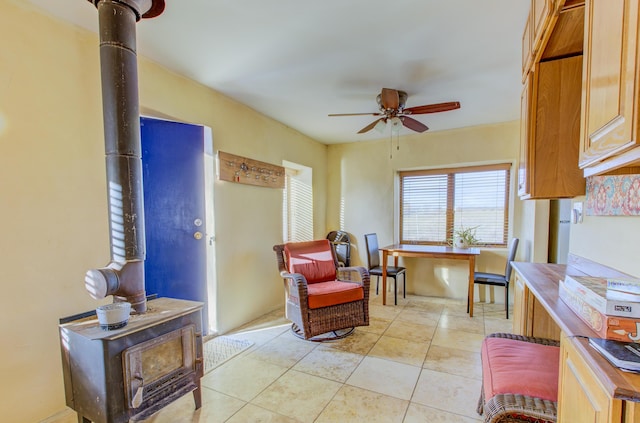 living area featuring light tile patterned floors, a wood stove, and ceiling fan