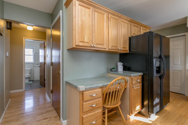 kitchen featuring light wood-type flooring, black fridge, and built in desk