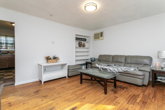 living room featuring a wall unit AC, baseboards, built in features, and wood finished floors