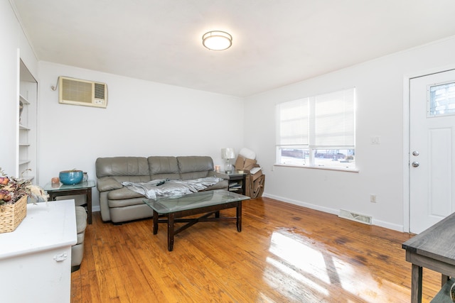 living area featuring a wall mounted air conditioner, visible vents, baseboards, and wood finished floors