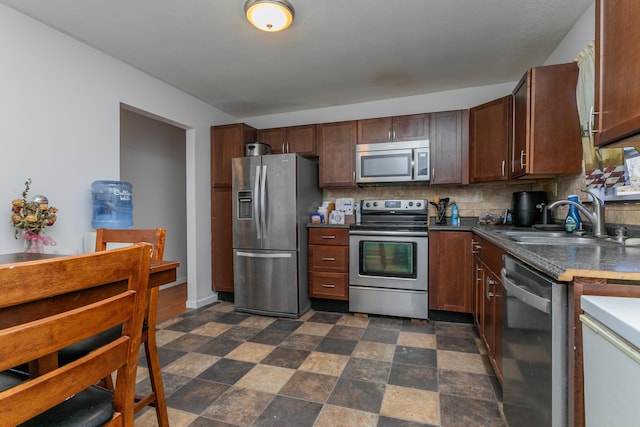 kitchen featuring stainless steel appliances, dark countertops, a sink, and tasteful backsplash