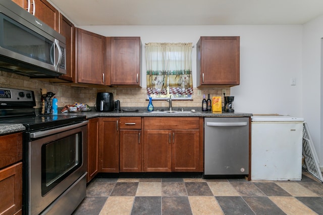 kitchen with decorative backsplash, dark countertops, appliances with stainless steel finishes, stone finish flooring, and a sink